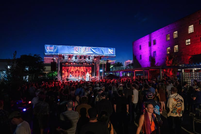 A large crowd of people at an outdoor event with a stage and a building in the background.